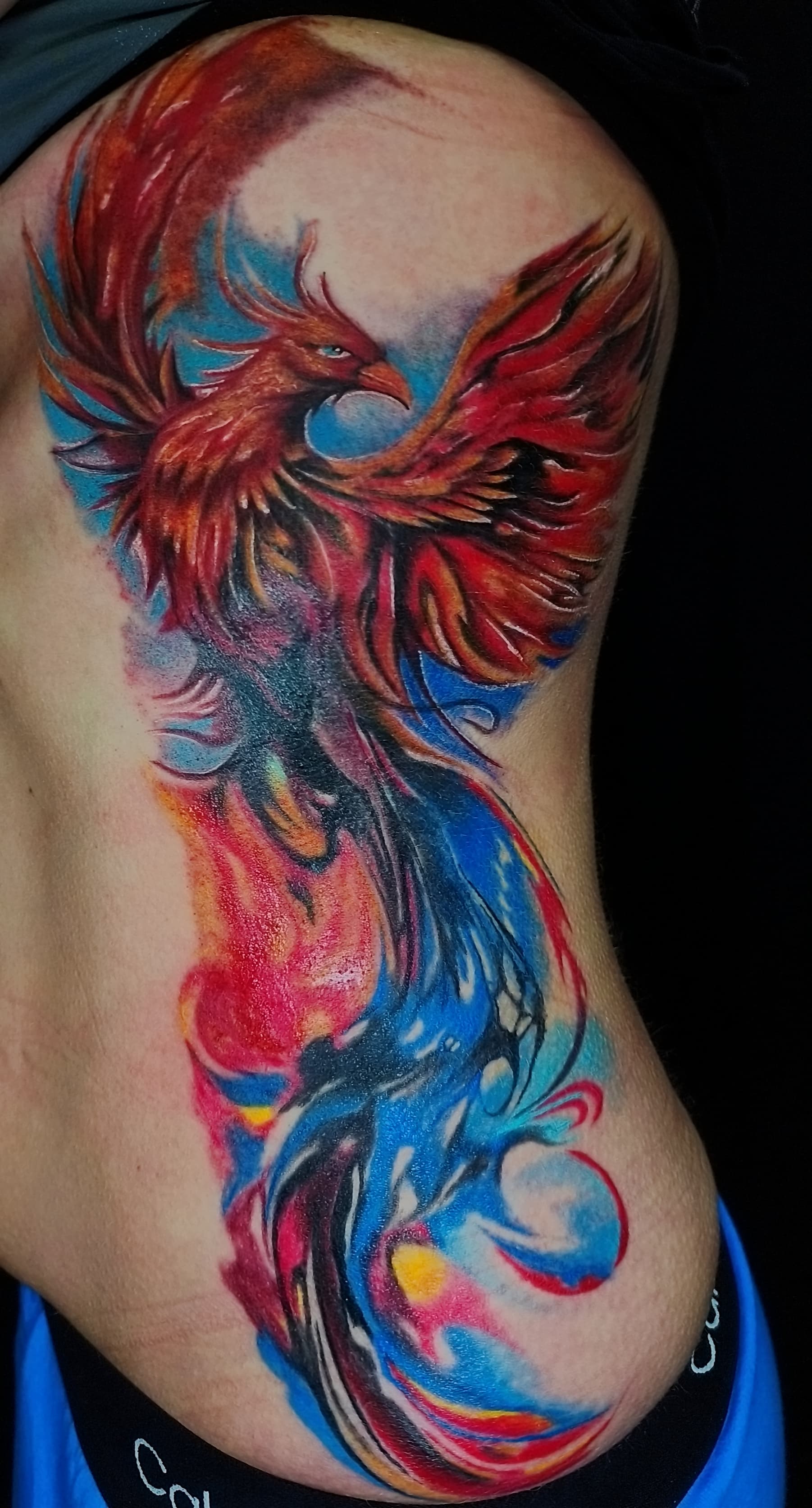 Kolorowy realistyczny tatuaz feniksa na boku ciała w odcieniach czerwieni, pomarańczu i błękitu